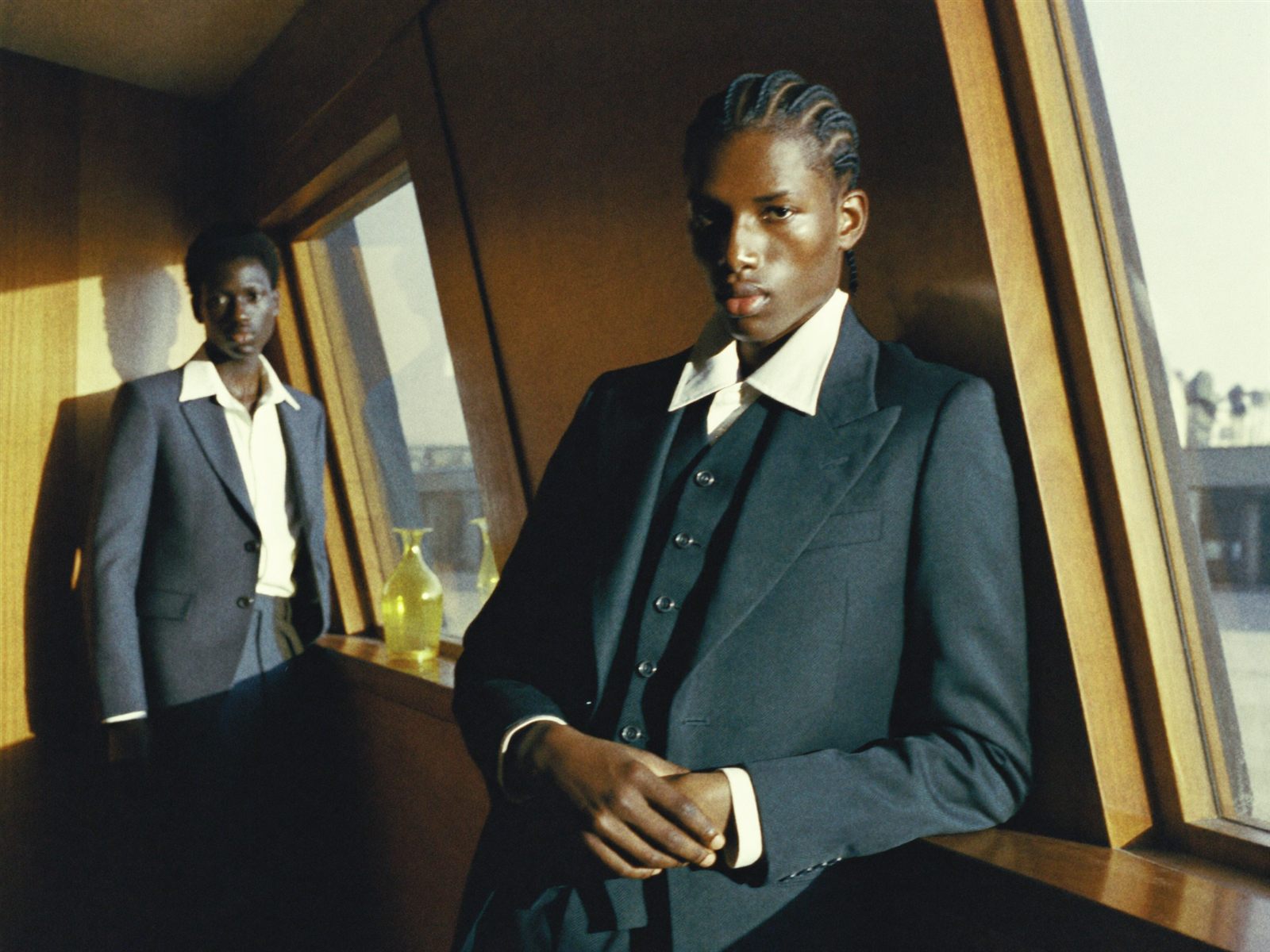 Two men in tailored suits by warm wood-panelled windows in afternoon light, a film-look editorial frame feeding the scopes below it